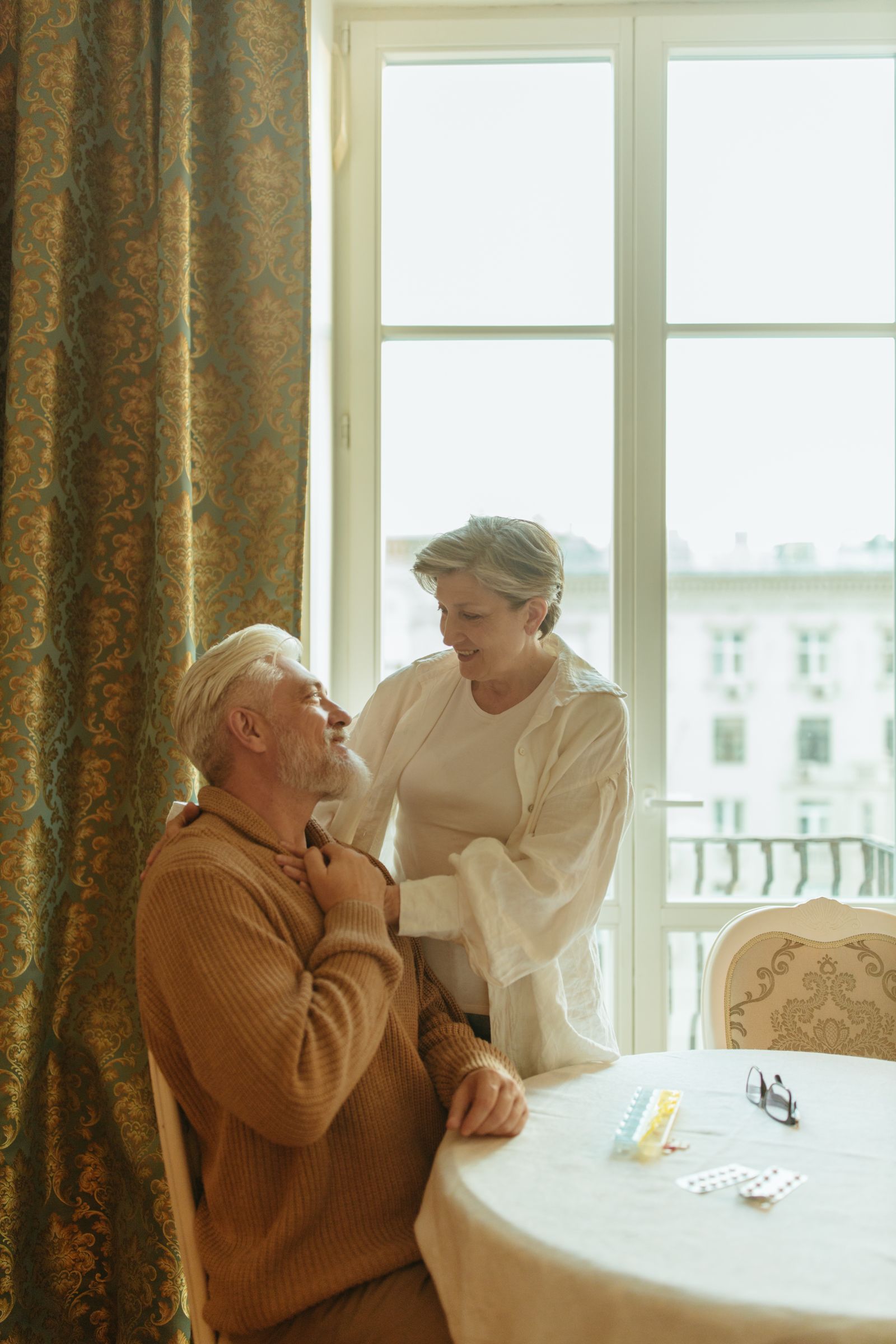 Elderly couple smiling at each other by a window